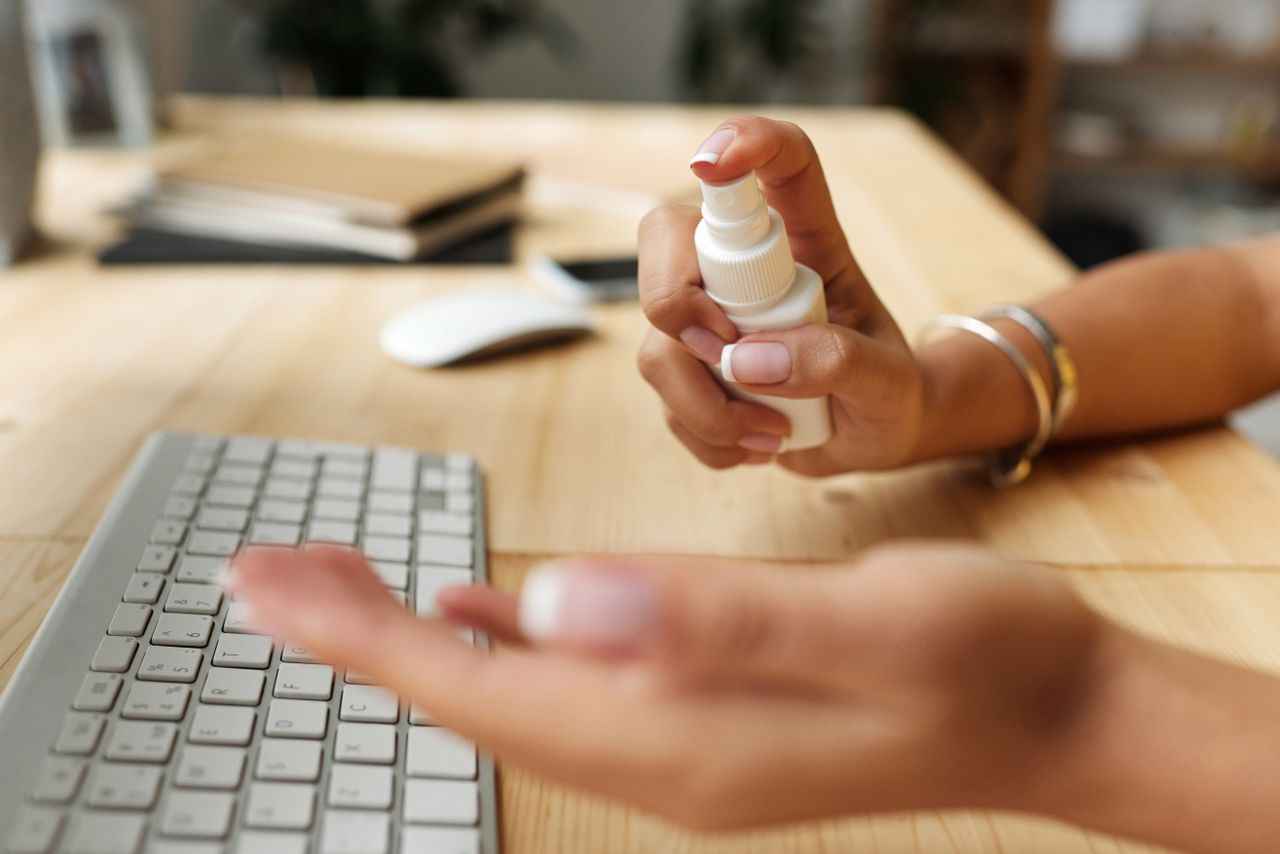 services-01 A person disinfecting their hands at a desk with a spray bottle, keyboard, and computer mouse.